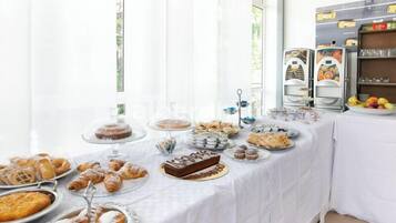 A buffet table with various baked goods and pastries, including croissants, muffins, and a cake.