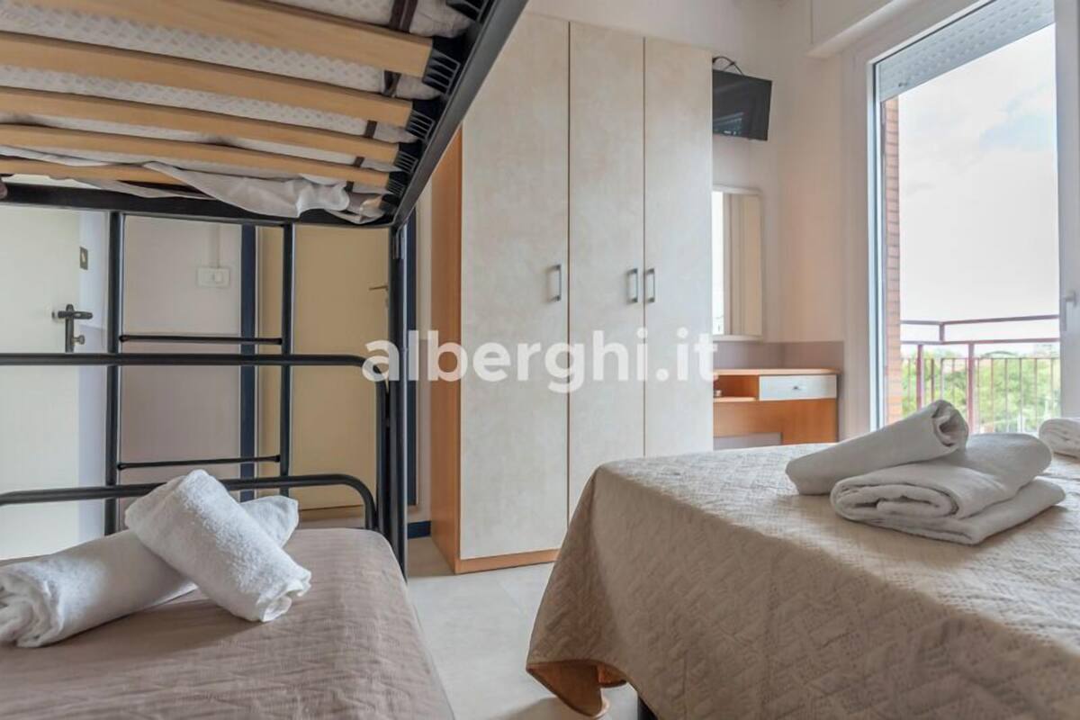 A hotel room with two beds, a wardrobe, a small table, and a balcony with a view.
