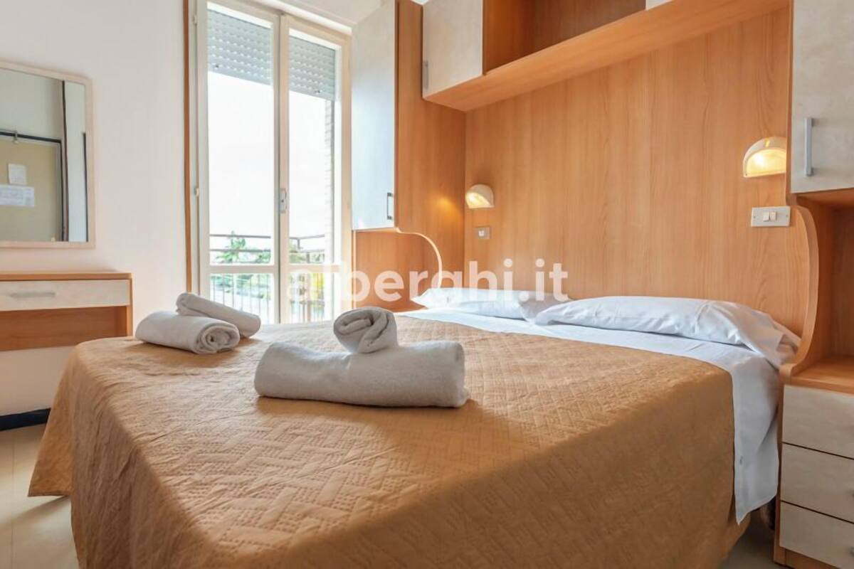 A hotel room with a bed, a nightstand, a mirror, and a window with a view.