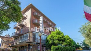 A multi-story hotel with balconies, a flag, and a clear sky. - hotel paradiso (Rimini)