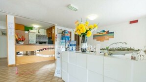 A reception area with a reception desk, a white counter, a vase with yellow flowers, and a wall with framed pictures. - hotel paradiso (Rimini)