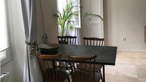 Ein Essbereich mit Tisch und Stühlen, einem Fenster mit Vorhängen und einer Zimmerpflanze.