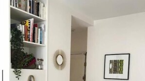 Ein Zimmer mit Bücherregal voller Bücher, einem kleinen hölzernen Hocker, einem gerahmten Bild an der Wand und einem Duschbereich.
