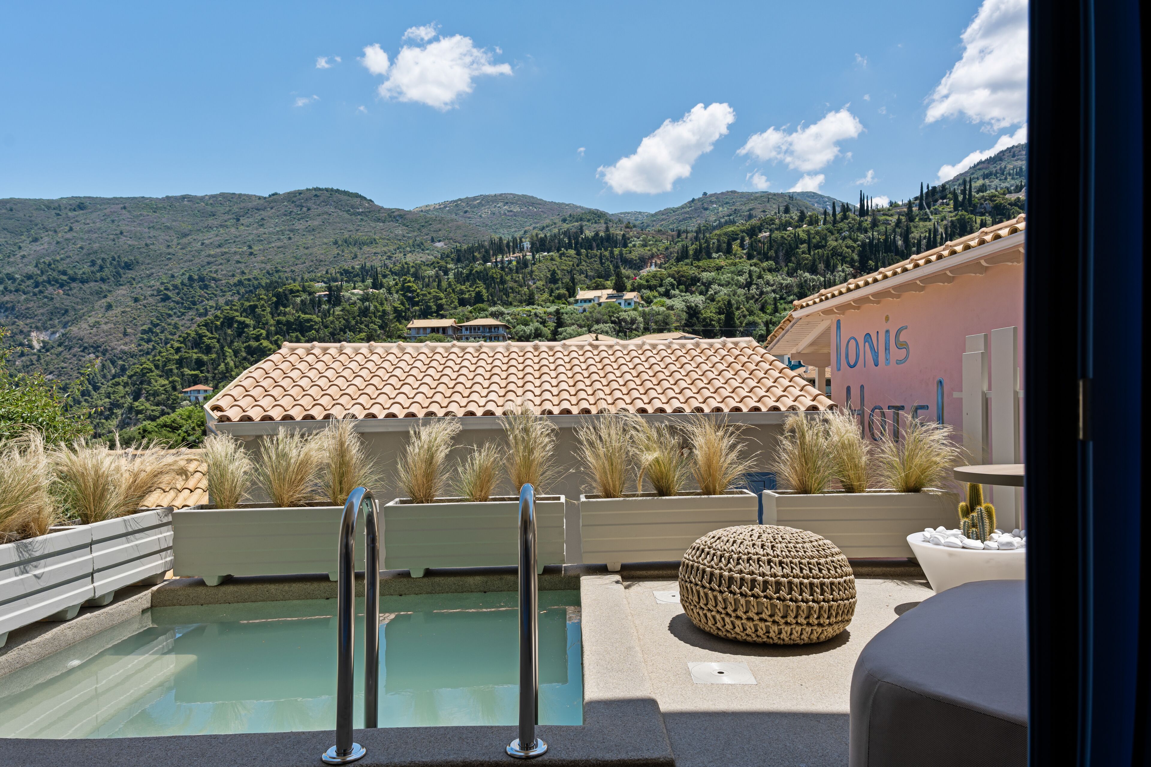 A pool area with a view of hills, a building with 'Ionia' written on it, and outdoor seating.