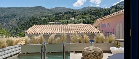 A pool area with a view of hills, a building with 'Ionia' written on it, and outdoor seating.