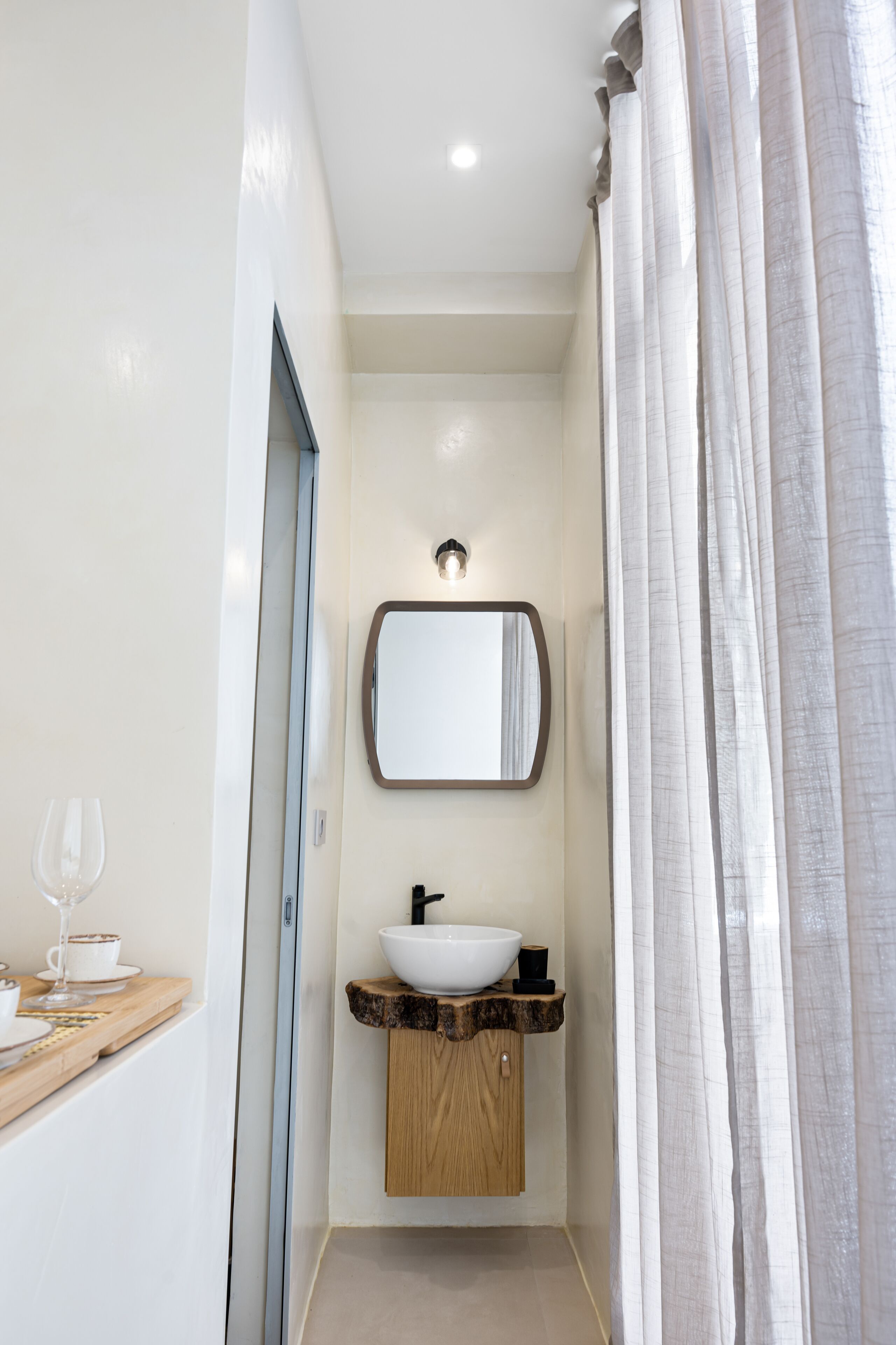 Un baño estrecho con un tocador de madera, un lavabo blanco y un espejo encima.
