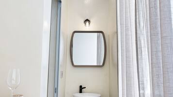 Un baño estrecho con un tocador de madera, un lavabo blanco y un espejo encima.