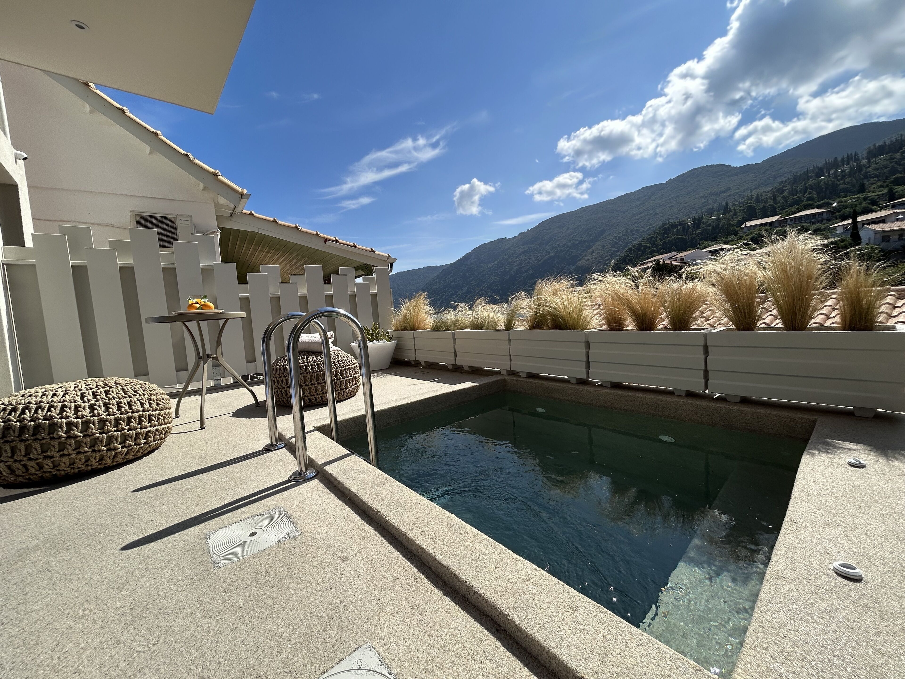 Un área de piscina con una valla blanca, una pequeña mesa con una silla y pastos altos.