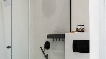 A modern bathroom with a glass-enclosed shower, a toilet, and a shelf with toiletries.