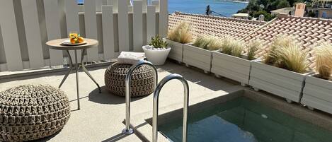 Zona junto a la piscina con vista al mar, valla blanca y mobiliario exterior.