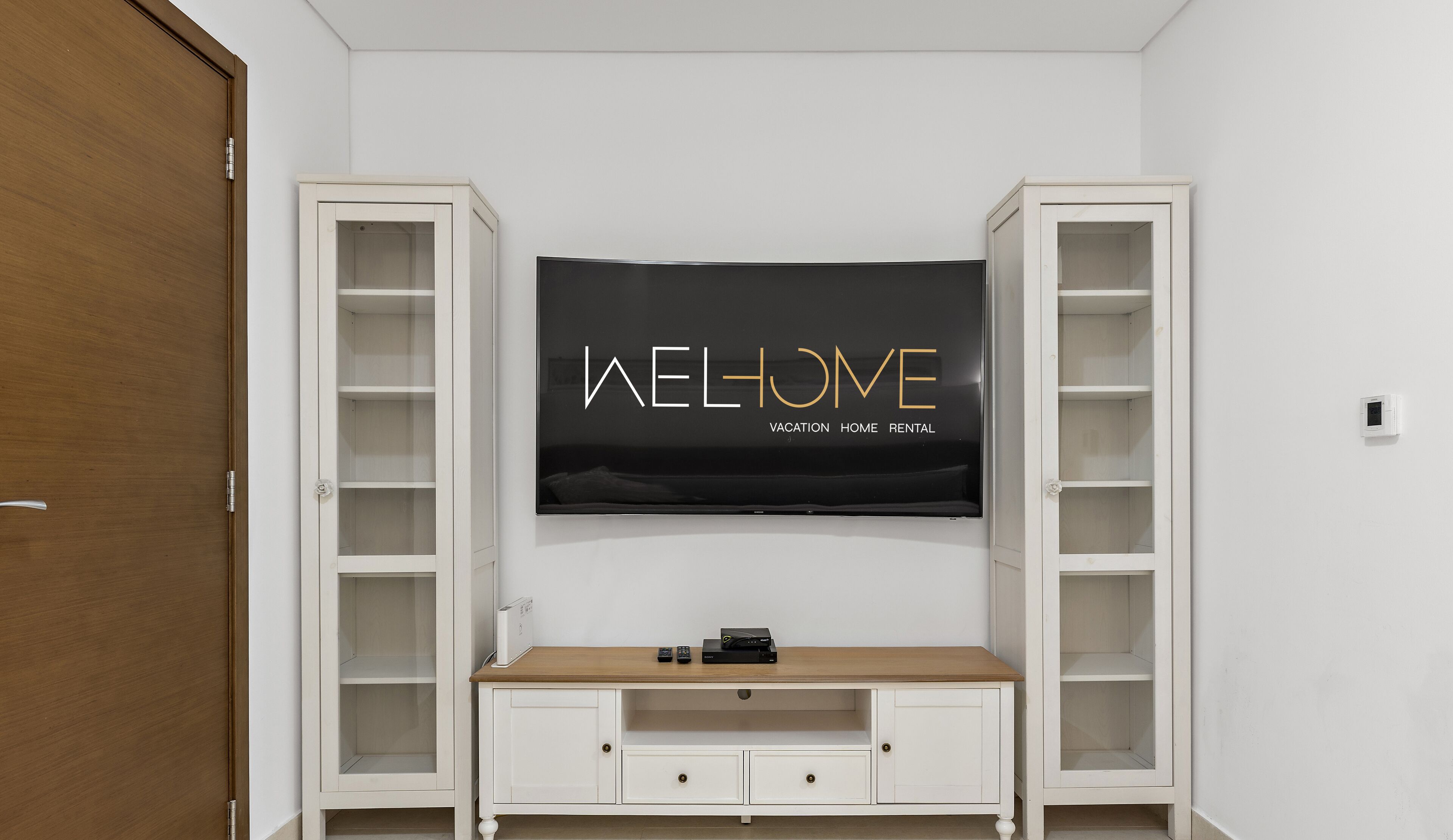 Una habitación con un televisor montado en la pared, un mueble bajo de madera y dos estanterías abiertas a cada lado.