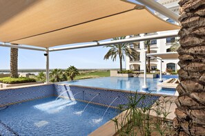 A pool area with a view of the ocean, a palm tree, and a building with balconies.