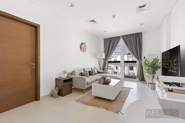 A modern living room with a sofa, coffee table, and TV. There is a door, a small cabinet, and a plant.