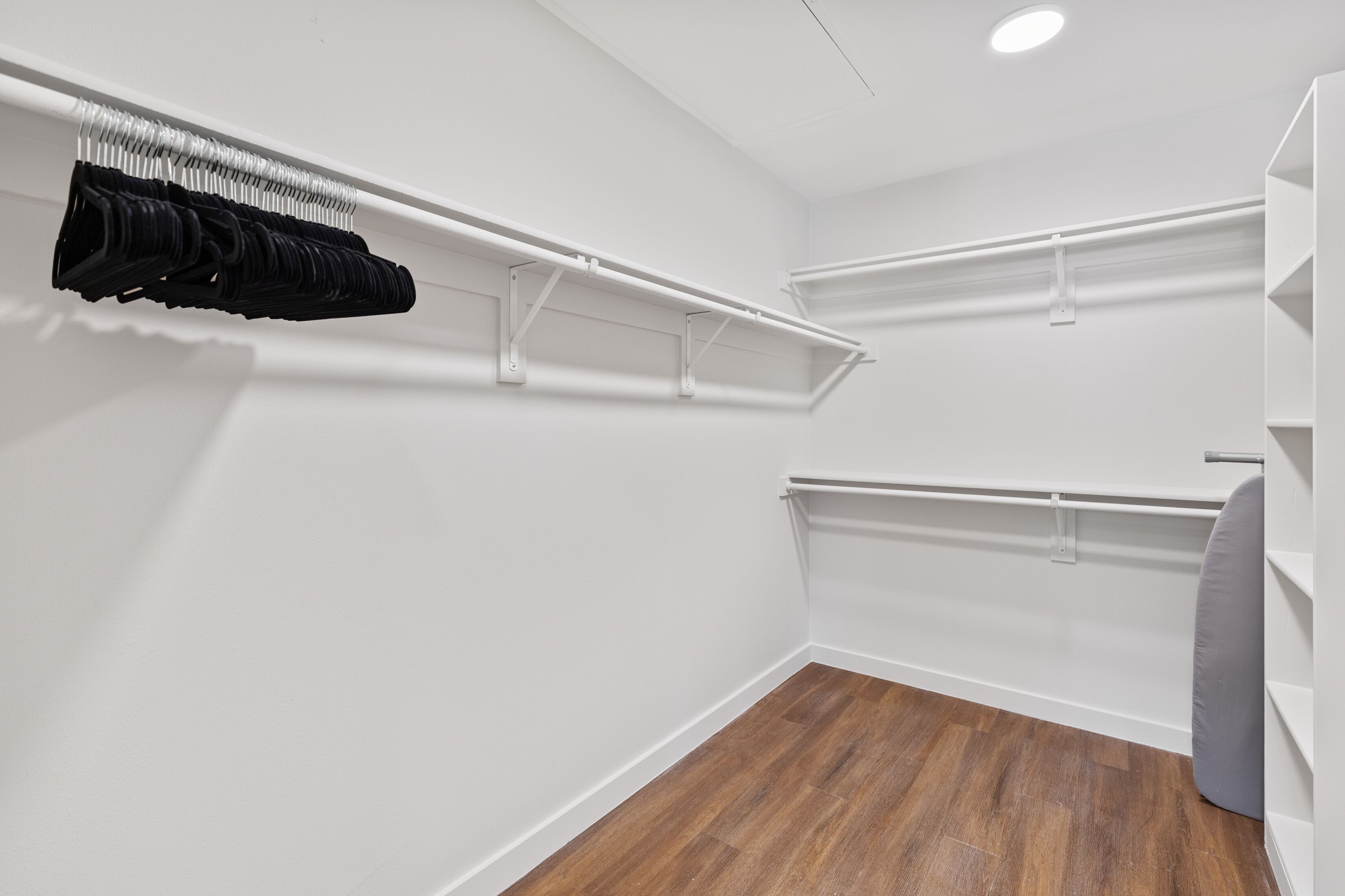 A walk-in closet with white shelving units and a wooden floor.