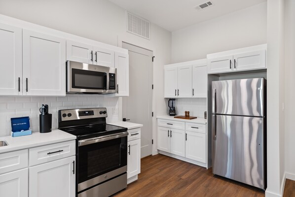 A modern kitchen with white cabinets, stainless steel appliances, and a wooden floor.