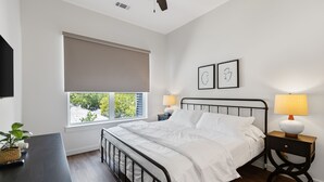 Ein Schlafzimmer mit einem Bett, zwei Nachttischen mit Lampen, einem Fenster mit Jalousie und einem Wandbild.