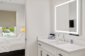 A hotel room with a bed, a bathroom with a sink, mirror, and toiletries.