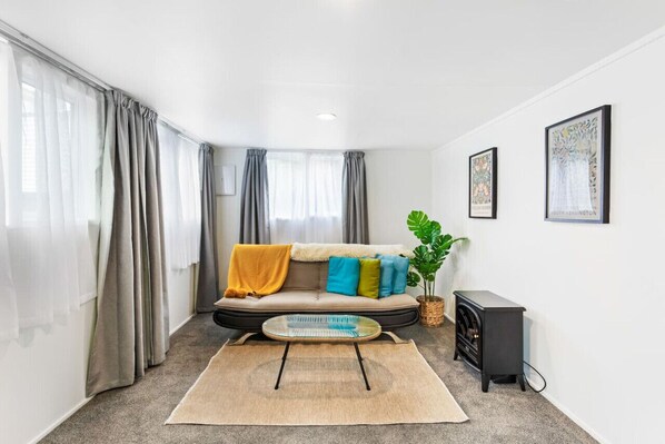 Relax in this stylish living room with a beige sofa, glass coffee table, and a small side table, surrounded by a lush green plant.