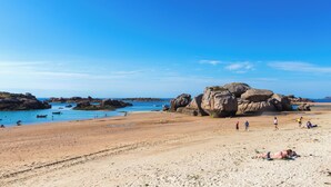 A beach with large rocks, clear blue water, and people sunbathing. - VVF Côte de Granit Rose à Trébeurden (Trébeurden)