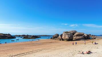 Ein Strand mit großen Felsen, klarem, blauem Wasser und sonnenbadenden Personen.