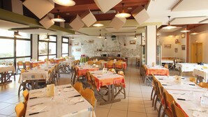 A dining area with tables set for meals, chairs, and hanging pendant lights. - VVF Côte de Granit Rose à Trébeurden (Trébeurden)