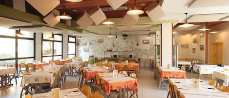 A dining area with tables set for meals, chairs, and hanging pendant lights.