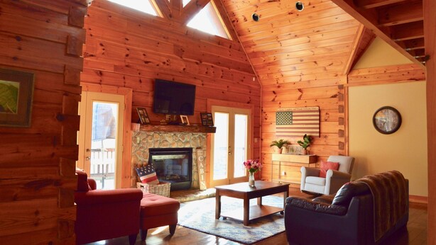 A log cabin interior with a fireplace, wooden walls, a television, and a cozy seating area. - Pines Cabin on Norris Lake (Tazewell)