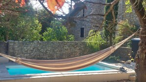 Eine Hängematte über einem Pool mit einer Steinmauer und Grünpflanzen im Hintergrund.