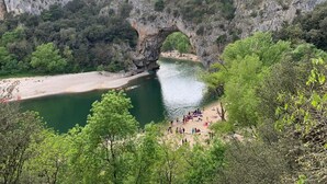 Ein natürlicher Felsbogen über einem Fluss mit einer Strandfläche im Vordergrund.