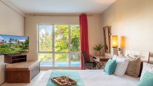 Een hotelkamer met een bed, een bureau, een televisie, een raam met uitzicht op groen en een lamp.