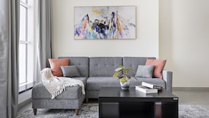 A modern living room with a grey sofa, a black coffee table, and a colorful abstract painting on the wall. - WelHome - Breathtaking Partial Sea View 2BR Close to Marina  (Dubai)