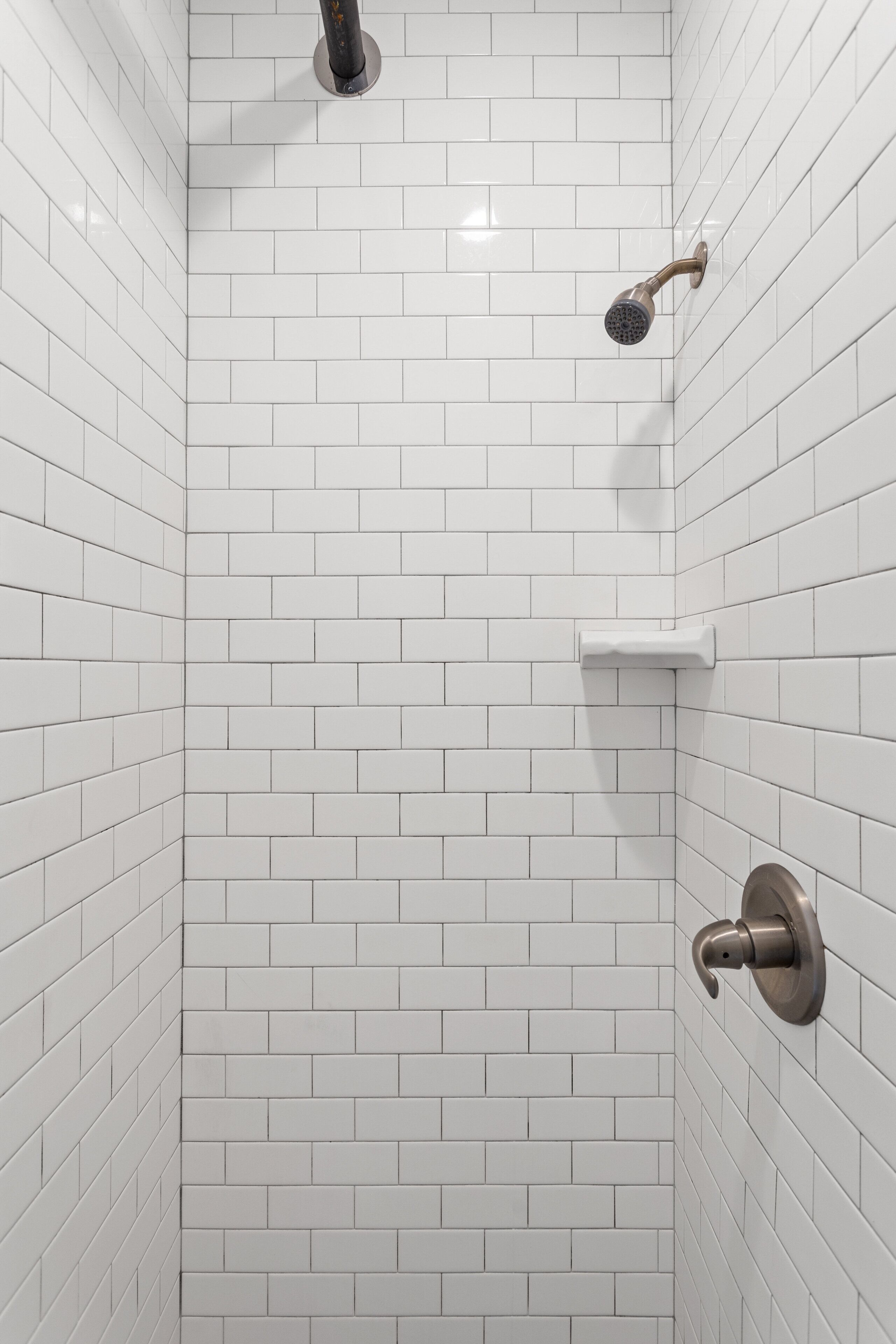 Une douche avec des murs recouverts de carreaux blancs et une pomme de douche chromée.