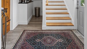 A modern interior with a staircase leading to a second floor, a kitchen area with a built-in shelf, and a patterned rug on the floor. - Guest House Topsail (Holly Ridge)