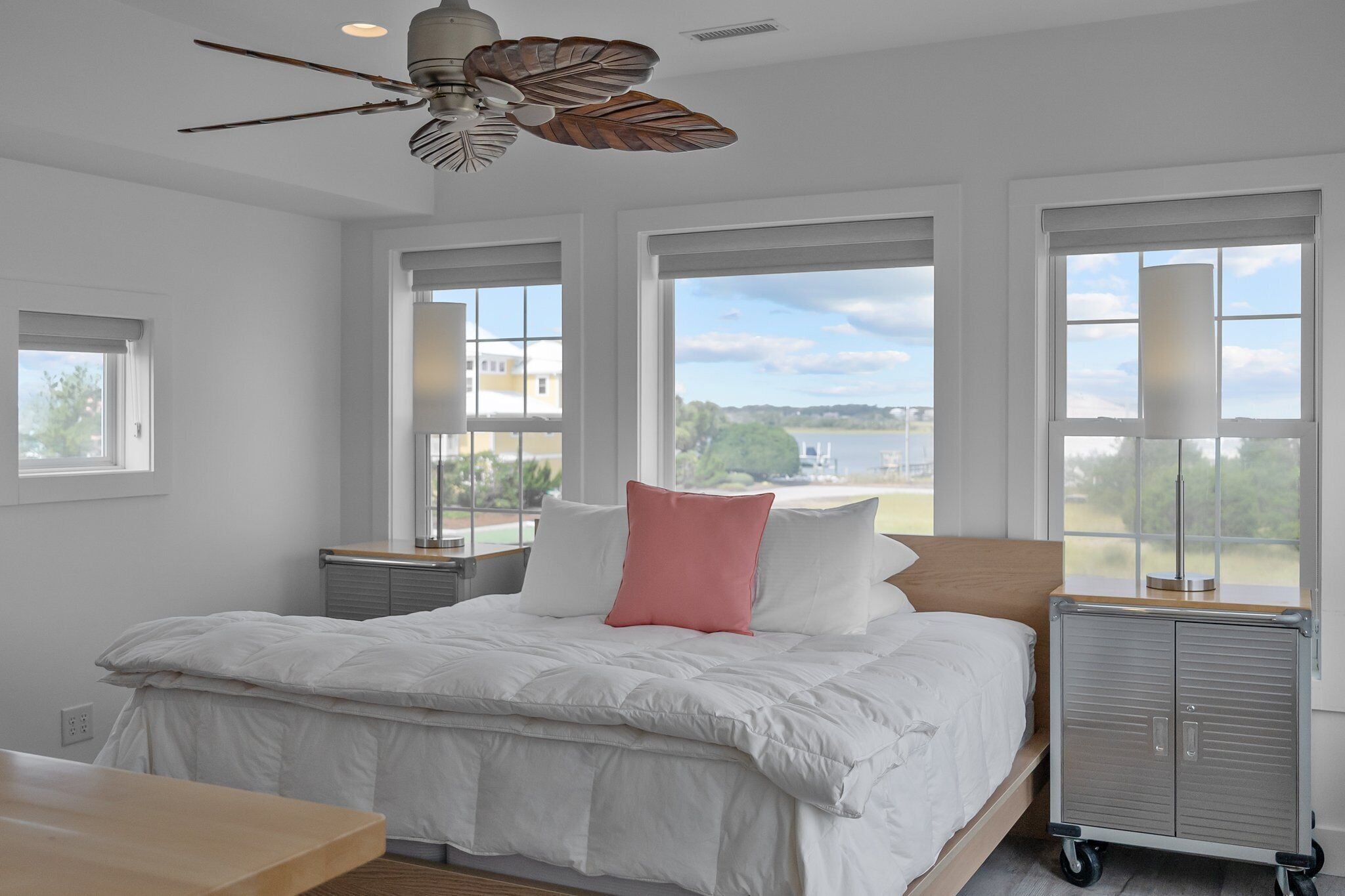 A bedroom with a large bed, a ceiling fan, and a view of a lake through the windows.