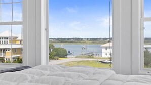 A bedroom with a large window overlooking a body of water, a dock, and buildings.