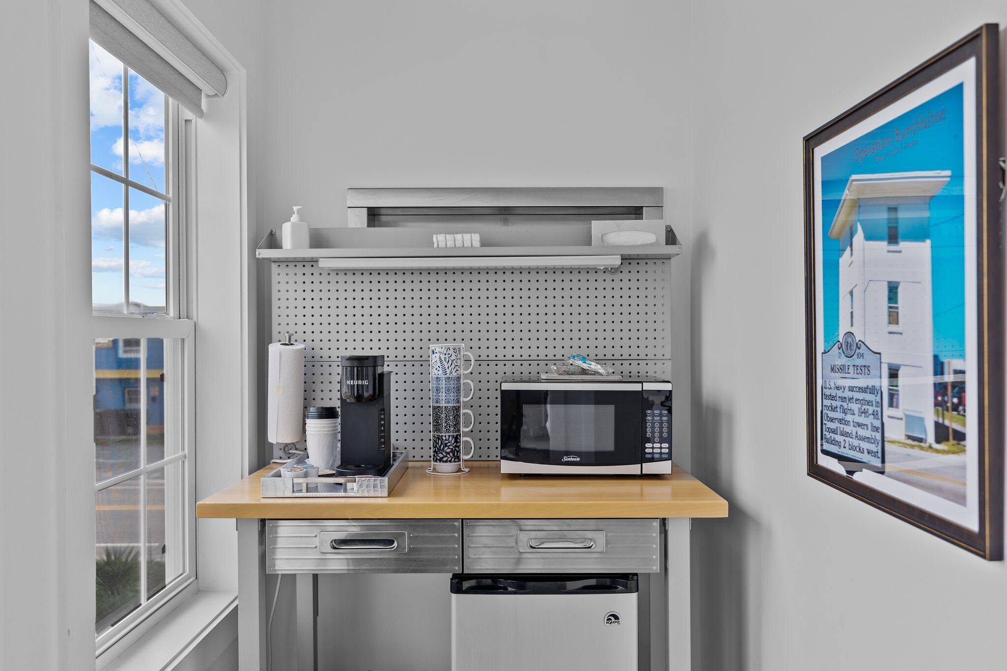 A kitchen with a microwave, coffee maker, and a framed picture on the wall.