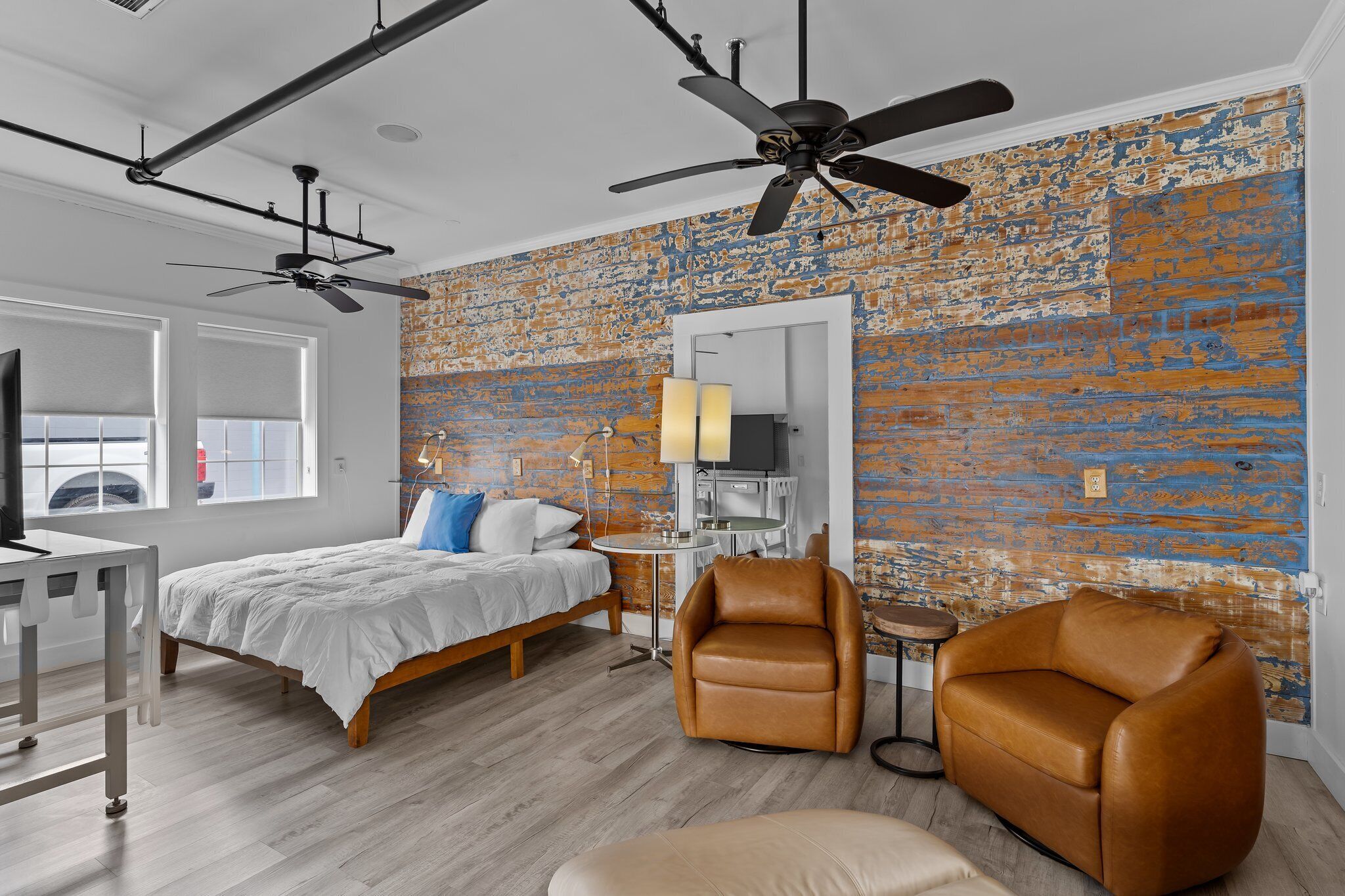A modern bedroom with a bed, two brown leather chairs, a small table, and a ceiling fan.