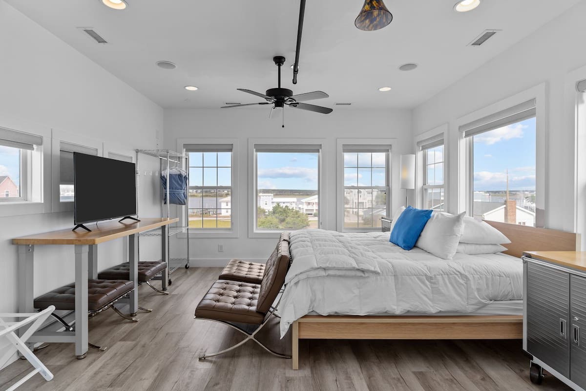 A modern bedroom with a bed, a desk, a chair, a TV, and a ceiling fan.
