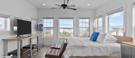 A modern bedroom with a bed, a desk, a chair, a TV, and a ceiling fan.