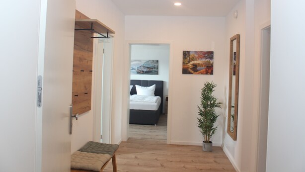 A hallway leading to a bedroom with a bed, a potted plant, and a painting on the wall. - 25 Minuten vom Großen Goitzschesee Entfernt, Apartment für bis zu Vier Personen (Zörbig)