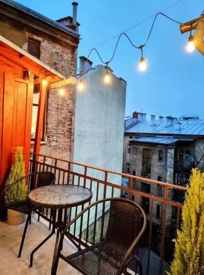 Relax and socialize in this charming outdoor space with a small table and two chairs, surrounded by string lights and a stone wall.