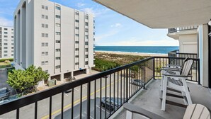 A balcony with a view of the beach and ocean, a parking area, and a building with multiple floors. - Ocean View North OC Oasis - Braemar Towers (Ocean City)