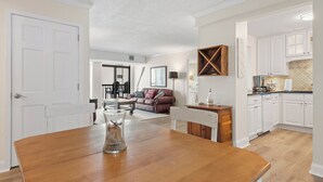 A spacious living room with a wooden dining table, a brown leather sofa, and a kitchen area with white cabinets. - Ocean View North OC Oasis - Braemar Towers (Ocean City)