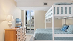 A bunk bed with a blue quilt, a wooden dresser with drawers, a lamp, and a window with blinds. - Ocean View North OC Oasis - Braemar Towers (Ocean City)