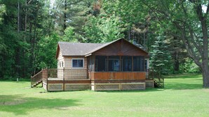 Une cabane en bois dotée d’un porche, entourée d’une pelouse et d’arbres.