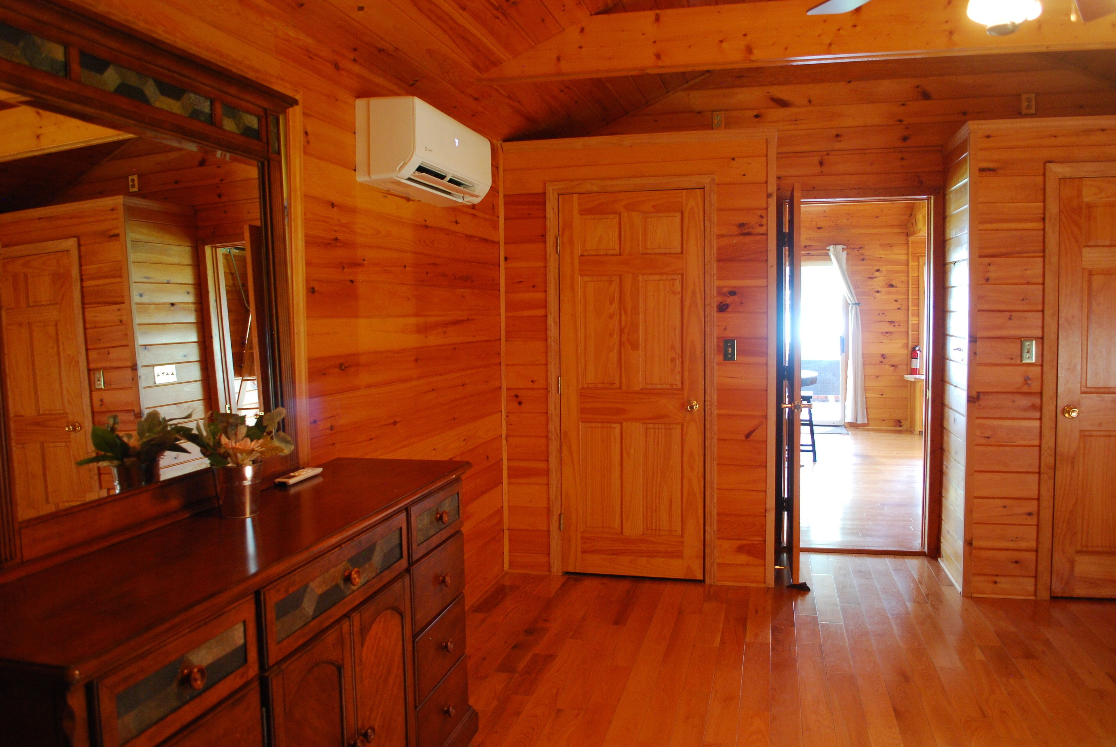 L’intérieur d’une cabane en bois, avec une commode en bois, un miroir et une porte donnant sur une autre pièce.