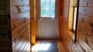 Un étroit couloir en bois, avec une porte au fond, une fenêtre au-dessus de la porte et un paillasson sur le sol.