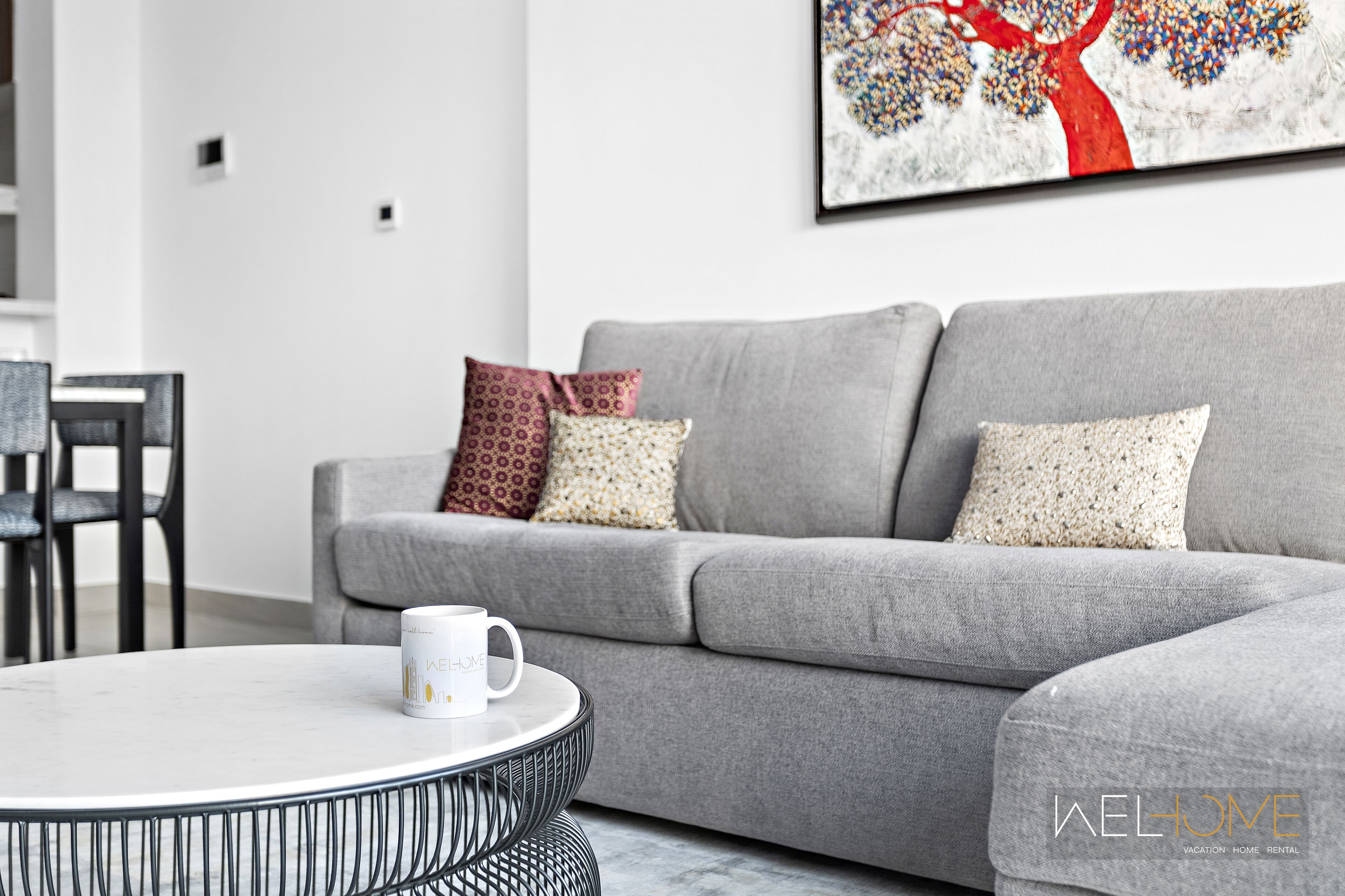 Een moderne woonkamer met een grijze bank, decoratieve kussens, een witte salontafel en een kunstwerk in een lijst aan de muur.
