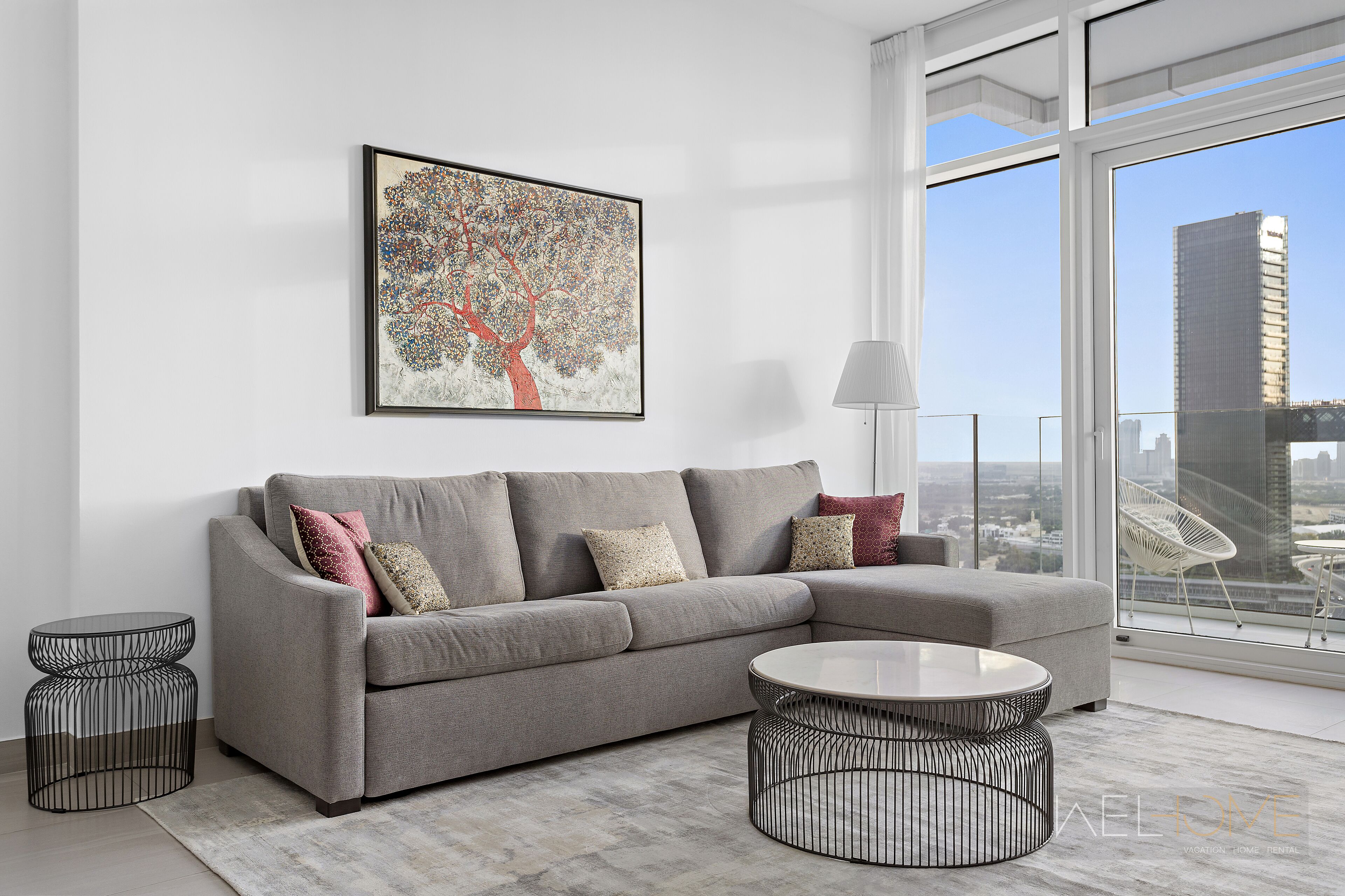 Een moderne woonkamer met een grijze hoekbank, een ronde salontafel en een gekaderd abstract schilderij aan de muur.