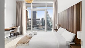 A modern hotel room with a large bed, a desk, and a view of the cityscape.